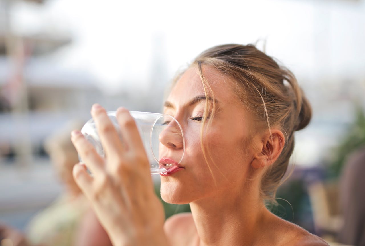 Close-up of a woman drinking water with a serene expression outdoors.